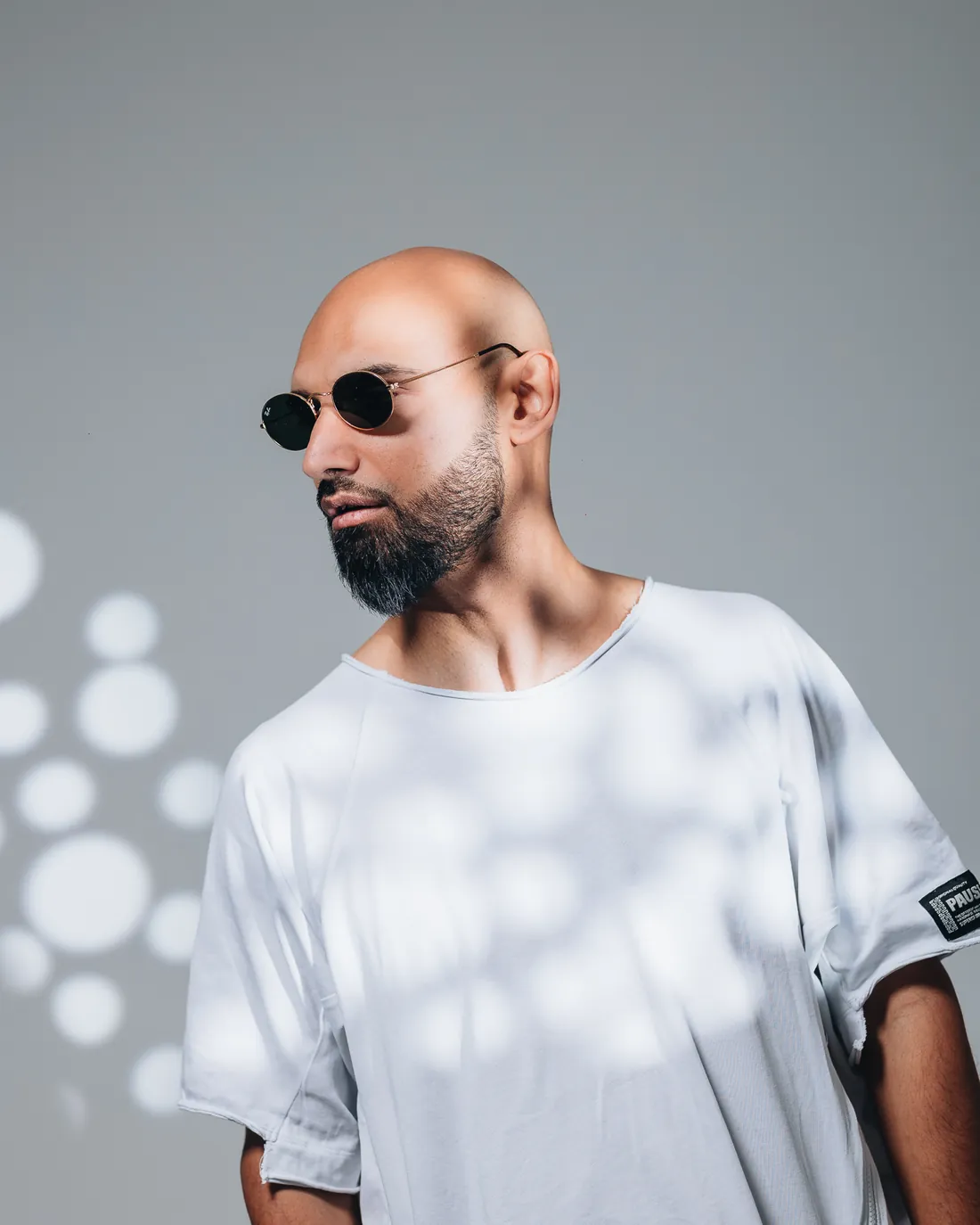 Bultech in sunglasses and a white T-shirt against a dotted light pattern